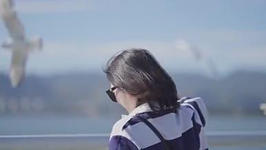 大景深下年轻女孩在海埂大坝喂海鸥唯美旅游视频的预览图